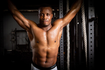 Fototapeta na wymiar Selective focus of young African athlete is doing exercise to build his biceps in a dark gym alone. African American man workouts by himself with bar in shadow tone background
