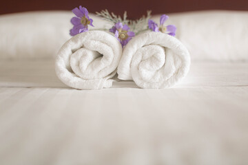Closeup of a set of white towel rolls on a hotel bed with purple flowers on them