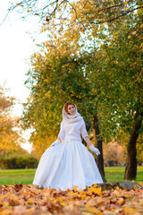 Portrait of a beautiful young redhead girl with flowers look attractive in a white dress on a background of autumn forest and leaves posing and smiling.