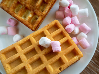 Appetizing cookies and other sweets on a plate close-up. Rectangular cookies with a beautiful texture have just been baked. White and pink little sweets lie nearby.