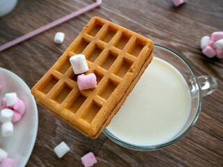On a wooden table, milk and sweets. On a cup with milk or milk drink lies a cookie. Background with milk, cookies and sweets for breakfast.
