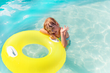 A little girl in the pool, on a Sunny day, swimming with tubing, waving her hand . An emotional...