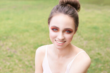Pretty young woman with red and orange bright makeup. Outdoor green portrait. park. Happy smile model face. Mascara artist style. Fashion smokey