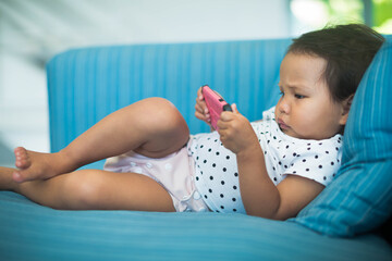 Chubby baby using a pink cell phone by herself on the sofa