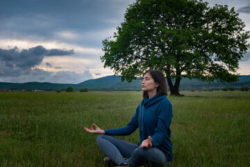 Naklejka na ściany i meble A young woman doing yoga in the field.
