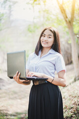 Obraz premium Asian young girl in school uniform are using laptop for education and communication at countryside of Thailand.