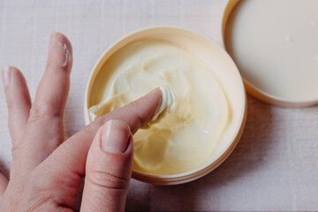 Skin and body care. Cream for the body, hands and feet, applied to the finger of a woman's hand on a natural white wooden background close-up with soft focus and a jar of cream in the background.