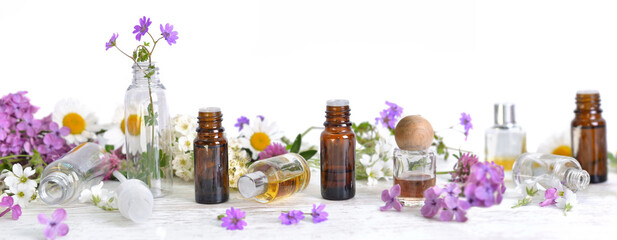 bottles of essential oil and colorful petals of flowers on white table in panoramic size