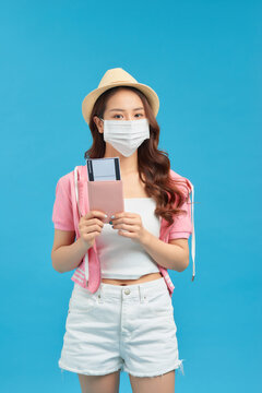 Young woman traveller wearing handmade cotton face mask with passport and ticket on blue background. Trip concept during coronavirus.