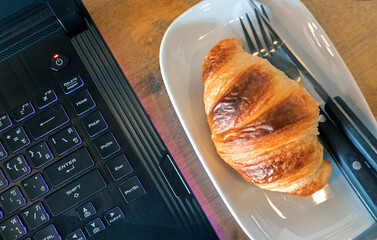 Croissant and notebook on table. Focus on the notebook device.