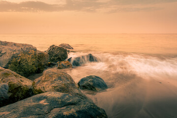 Beautiful golden sunset over the sea of Oman, with waves and rocks.