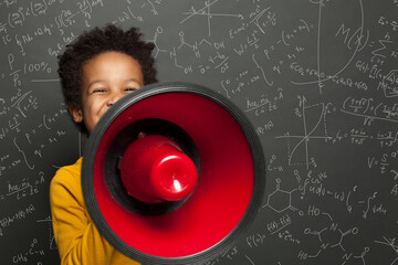 Smart black child with megaphone loudspeaker on chalkboard background with science formulas