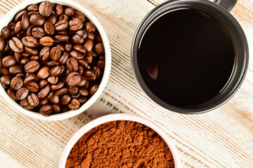 Close-up coffee beans, coffee powder and ready coffee in the mugs on wooden table.