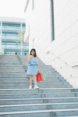 Asian young woman going down stairs and holding shopping bags in hand, shopaholic concept