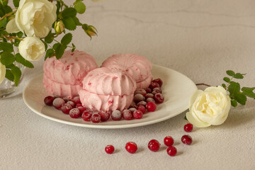 Marshmallows with cranberries on the table. Nearby is a vase with rose flowers.