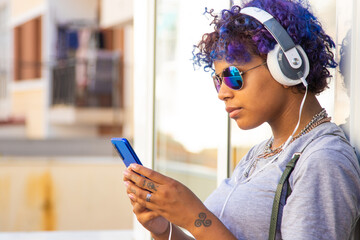 afro american latin girl with mobile phone and headphones on the street outdoors