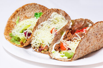 3 tacos . Mexican food created with tortillas, cream cheese, cooked chopped meat, avocado sauce, lettuce and tomato salad, with cheese on top. 
detailed look