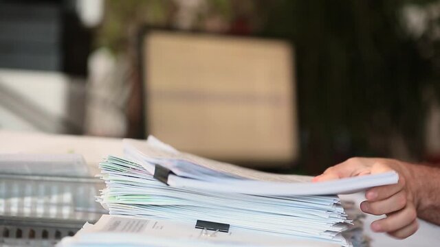 A man parses papers in the office and stacks them in a pile - focus on a stack of papers.