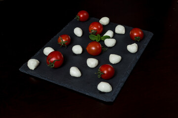 Pattern of mini balls of mozzarella cheese and cherry tomatoes on a stone plate