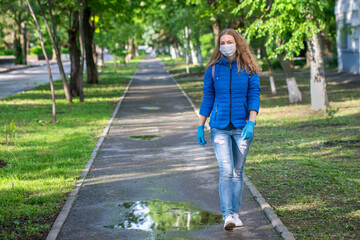 Fototapeta premium A Caucasian blond woman in a protective mask and gloves is walking on empty the street. Prevention of viral infection. Responsible social behavior of a citizen in a public place. Copy space