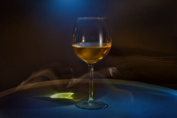 White wine in a glass on the table on a creative black background. Cigarette smoke in the bar and an alcoholic drink at a party or disco. Shooting in the dark key. Copy space