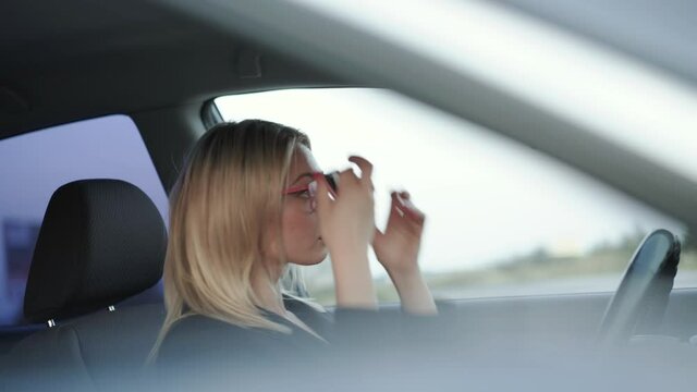 Blonde in glasses corrects hair and applying the red pomade at mirror in the car