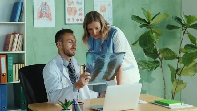 Couple of caucasian doctors examining fluorography x-ray scan of lungs in hospital. Scared nurse leaving the doctor cabinet after embarrassing sexual harassment. Bullying at work.