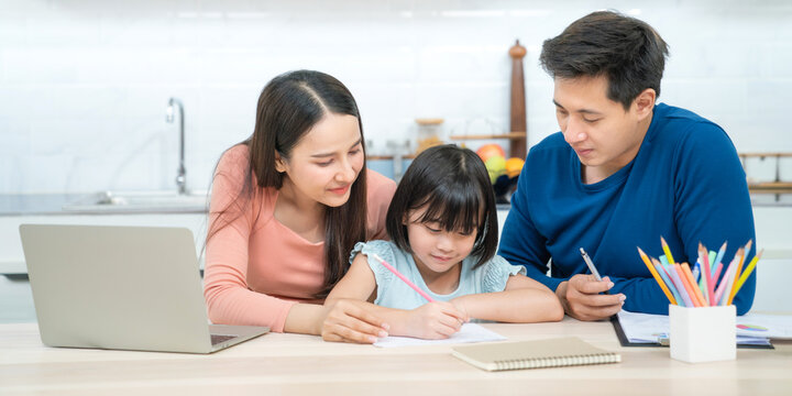 Father and mother teaching children to do their homework at home. Happy asian family using the laptop together at home. Young asian family parents helping daughter drawing at home