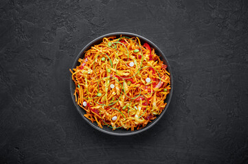 Chinese Bhel in black bowl on dark slate table top. Chinese Bhel is Indo-Chinese cuisine street food dish of deep fried hakka noodles, vegetables and schezwan sauce