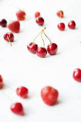 Vertical photo of strawberries and cherries scattered on a white table. Triple cherry branch.