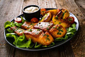 Fried salmon steak with potatoes and vegetables served on black plate on wooden table