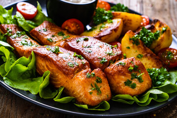 Fried salmon steak with potatoes and vegetables served on black plate on wooden table