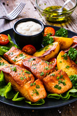 Fried salmon steak with potatoes and vegetables served on black plate on wooden table