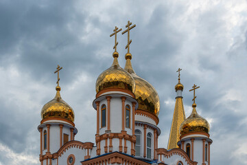 Fototapeta na wymiar Golden domes of a snow-white Christian church against a disturbing cloudy blue summer sky
