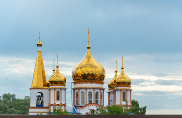 Snow-white Christian church with golden domes against a calm blue summer sky