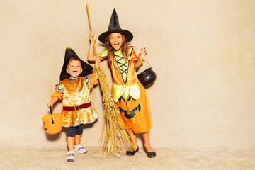 Two kids brother and sister in Halloween costumes with broom, candy buckets stand over wall show spooky gestures