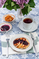 On the table is a cup of tea and pancakes with jam.