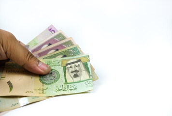 Image of man's fingers holding saudi riyal notes in SR1, SR5, SR50 and SR 100 over white. Focus on...