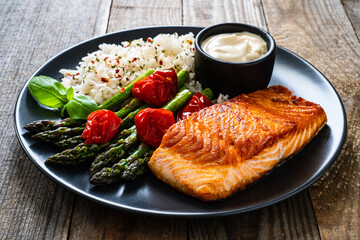 Fried salmon steak with rice and asparagus served on black plate on wooden table
