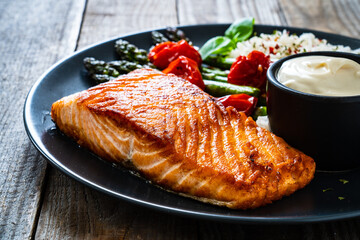 Fried salmon steak with rice and asparagus served on black plate on wooden table
