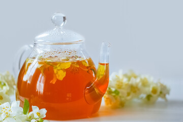 glass teapot with hot tea and Jasmine flowers. background with a teapot with tea and branches of blooming Jasmine.