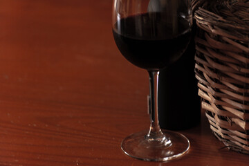 old wicker jerrycan of wine with its bottle and glass of wine on wooden table