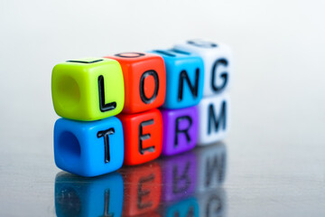 Conceptual non-current liabilities due beyond a year or the normal operation period of the company. Alphabet beads LONG TERM LIABILITIES on reflective surface.
