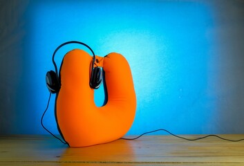 Conceptual image of holiday season. Earphones attached to orange neck pillow on wooden surface. Blue background. Focus on ear piece on right. Others in gradient blur.