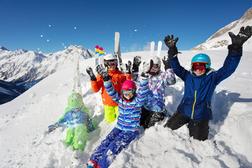 Portrait from above of kids sit together throw snow in the air over beautiful mountain range tops in Alps