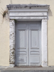 Fototapeta na wymiar Gray colonial door with worn white stone frame and broken facade. Tropical architecture and construction detail.