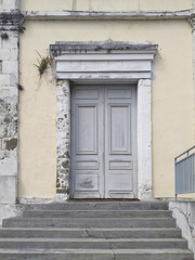 Fototapeta na wymiar Stairs and old colonial facade with gray door with worn white stone frame and broken facade. Tropical architecture and construction detail.