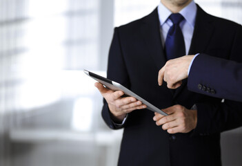 Business people use a tablet computer for discussion of their new project, standing in a modern office. Unknown businessman or male entrepreneur with a colleague at workplace. Teamwork and partnership