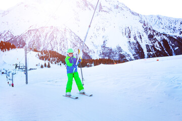 Happy little boy lifting on the ski drag lift rope in bright sport outfit over sunset light near...