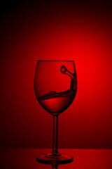 A splash of red wine in a glass on a red background